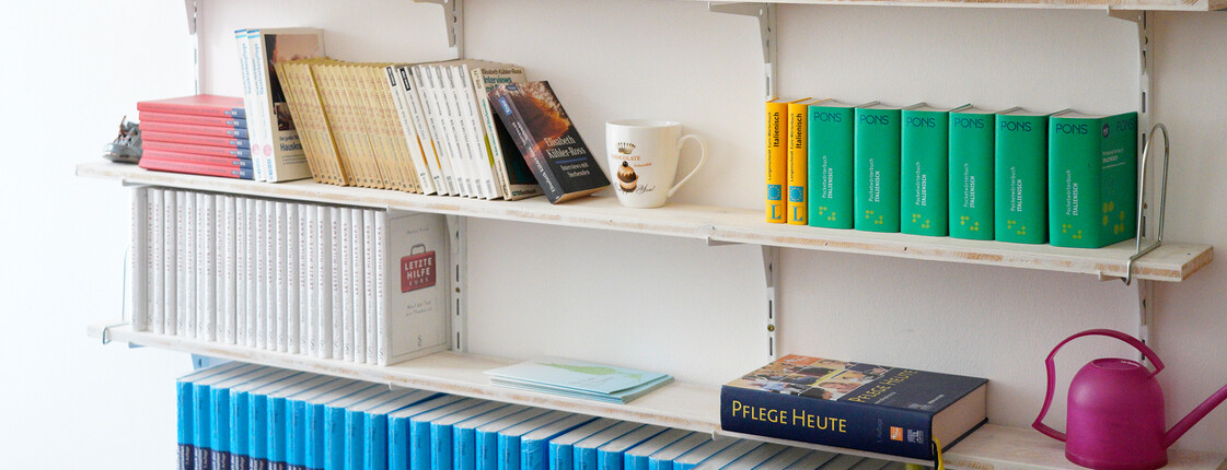Bücher stehen auf weißen Regalen an der Wand.